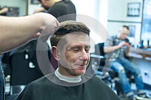 Smiling man, client in a barbershop, closing his eyes, enjoys th