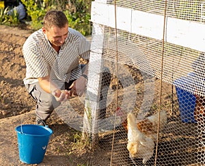 Smiling man collecting eggs of chickens in coop on backyard