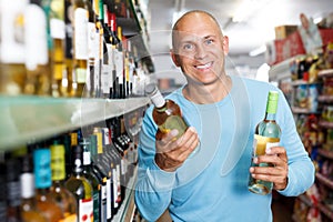 Smiling man customer looking bottle of white wine in supermarket