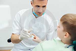 Smiling man dentist showing dental jaw model to little boy
