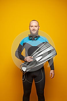 Smiling man diver standing holding fins on bright yellow studio background