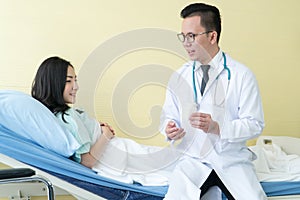 Smiling man doctor holding pill bottle and consulting woman lying bed in hospital