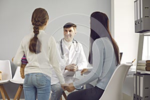 Smiling man doctor pediatrician listening to small girl and mother patients complaints