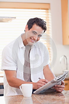 Smiling man doing crossword puzzle in the kitchen