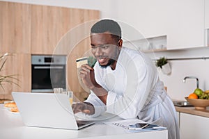 Smiling man doing online shopping and standing with credit card