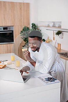 Smiling man doing online shopping and standing with credit card