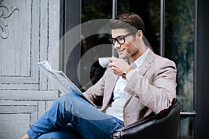 Smiling man drinking coffee and reading magazine in outdoor cafe