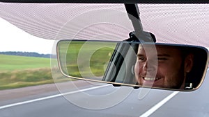 smiling man driver reflection in car rear view mirror