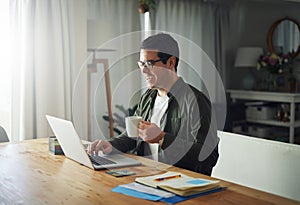 Smiling man enjoying the coffee while using laptop at home