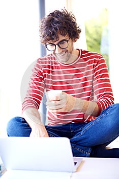 Smiling man with eyeglasses using his laptop and drinking tea at home