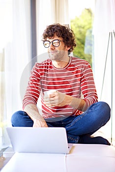 Smiling man with eyeglasses using his laptop and drinking tea at home