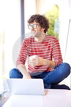 Smiling man with eyeglasses using his laptop and drinking tea at home