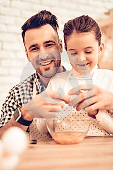 Smiling Man with Girl Break Eggs in Bowl at Home.