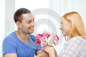 Smiling man giving girfriens flowers at home