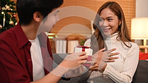 Smiling man giving surprise gift to his girlfriend, celebrating Christmas at home. Family, holidays and people concept