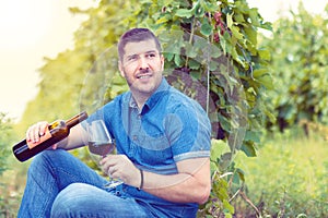 Smiling man having fun holding a glass of red wine in hand at sunset in vineyard