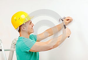 Smiling man in helmet hammering nail in wall