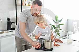 smiling man helping his son using mixer for making dough