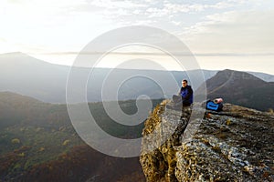 Smiling man hiker with backpack siting and relaxing on the top of the mountain and looking at beautiful yellow autumn