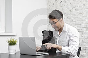 Smiling man and his lovely pet pug working on laptop at home