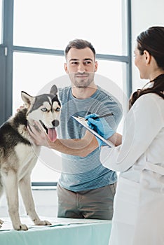 smiling man holding husky and female veterinarian writing