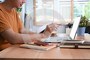 Smiling man holding notebook and using laptop computer a home.