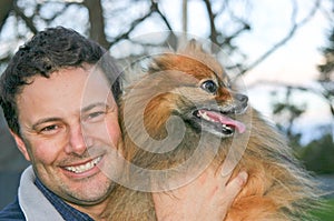 Smiling man holding a Pomeranian dog on his shoulder