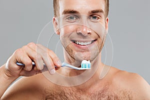 Smiling man holding toothbrush with toothpaste and cleaning his teeth