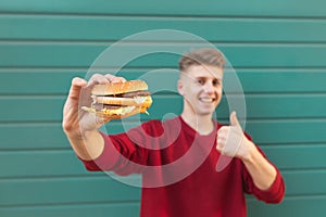 Smiling man holds an appetizing burger in his hands and shows a thumbs up. Fast food
