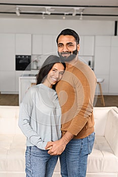 Smiling man hugging his charming woman. Two people standing and joyfully looking at the camera. Young Indian couple