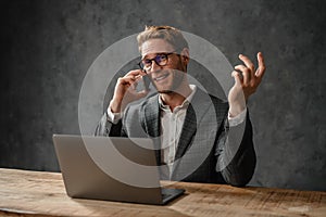 The smiling man in a jacket and shirt talking on the phone and spreading his hands