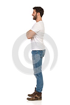 Smiling Man In Jeans And White T-shirt Is Standing With Arms Crossed. Side View