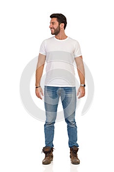 Smiling Man In Jeans And White T-shirt Is Standing And Looking Away. Front View