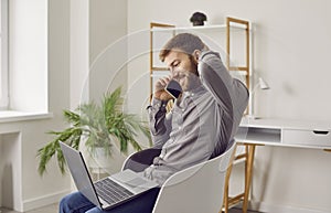 Smiling man with laptop talking on mobile phone, sitting in chair at home or at office.