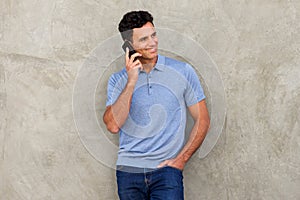 Smiling man leaning against wall and talking on mobile phone