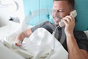 Smiling man lies in bed and talks on phone