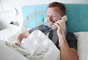 Smiling man lies in bed and talks on phone