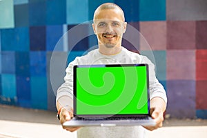 Smiling man looking in camera and holding laptop with chromakey green screen