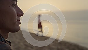 Smiling man looking sea landscape at sunrise. Positive guy sitting on beach