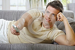 Smiling man lying on sofa watching television