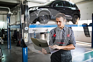 Smiling man mechanic using a laptop computer to check a car engine