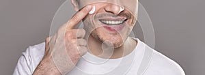 Smiling man moisturizing face with crea,. close up portrait