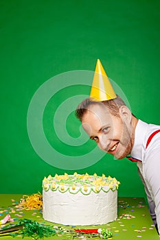 Smiling man in party hat with birthday cake in studio