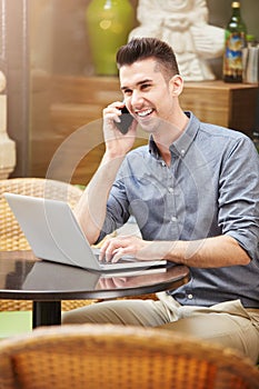 Smiling man on phone call at cafe with laptop