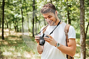 Smiling man photographer using modern photo camera in forest