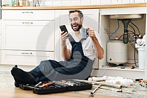 Smiling man plumber using mobile phone drinking coffee