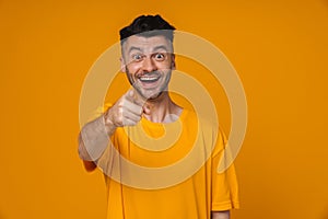 Smiling man pointing finger at camera isolated over yellow background