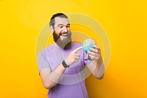 Smiling man is pointing on a small globe over yellow background. photo