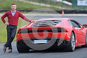 Smiling man posing against red sport car on circuit