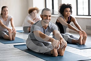 Smiling man practicing yoga at group lesson, Seated forward bend